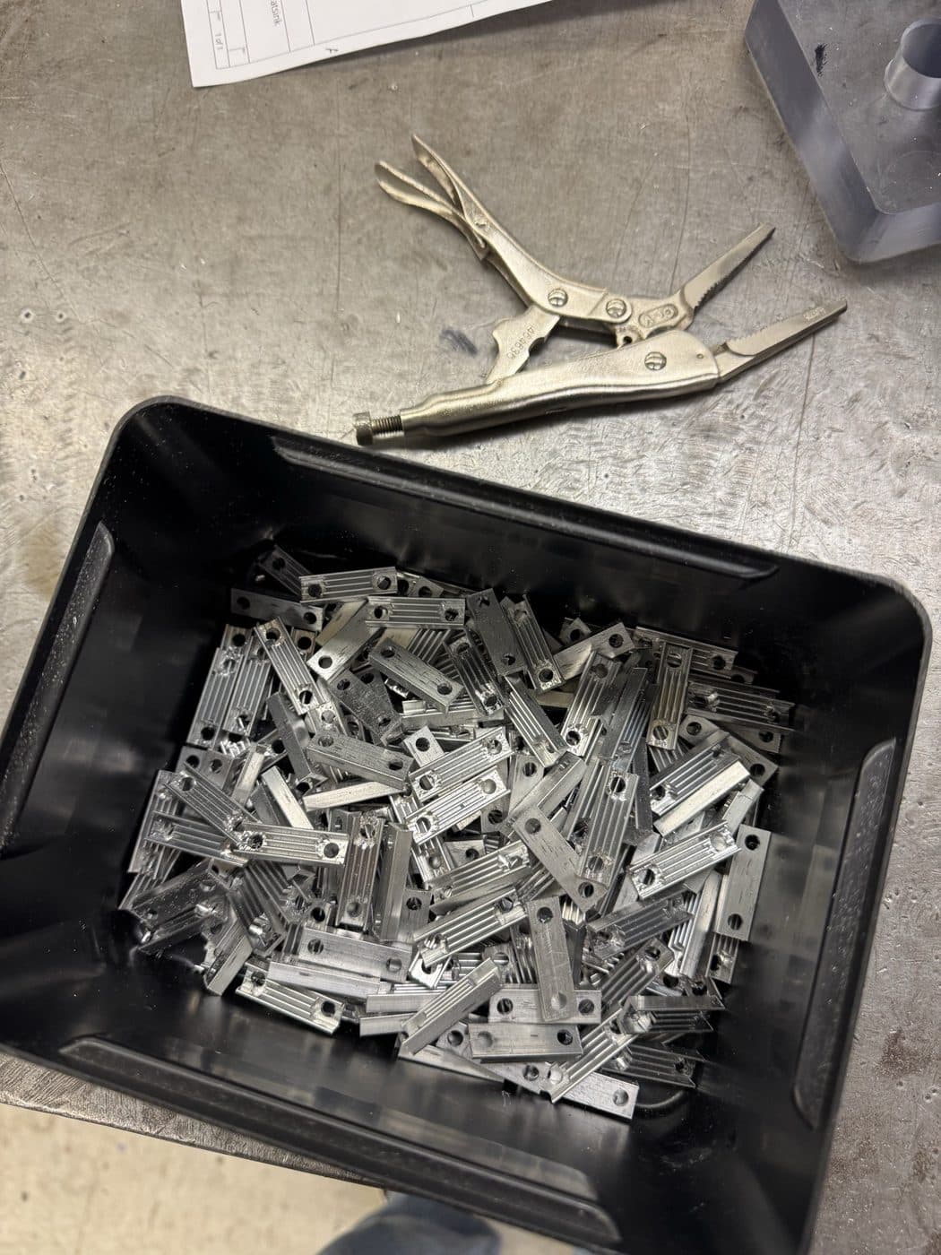 A production run of machined brackets in a bin, ready for inspection.