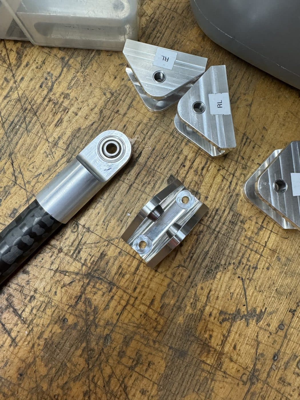 Machined aluminium rocker and clevis brackets with a spherical rod end and carbon-fibre tie rod, hand-labelled left and right before assembly.