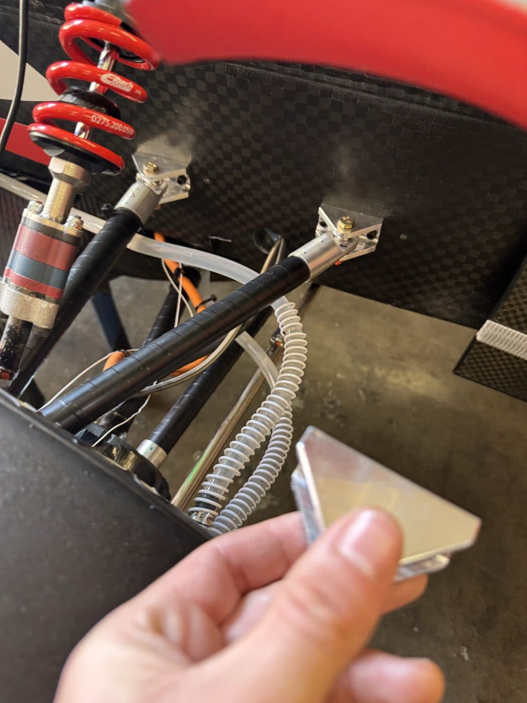 Trial fit of a machined bracket against the installed pushrod and damper on the car.