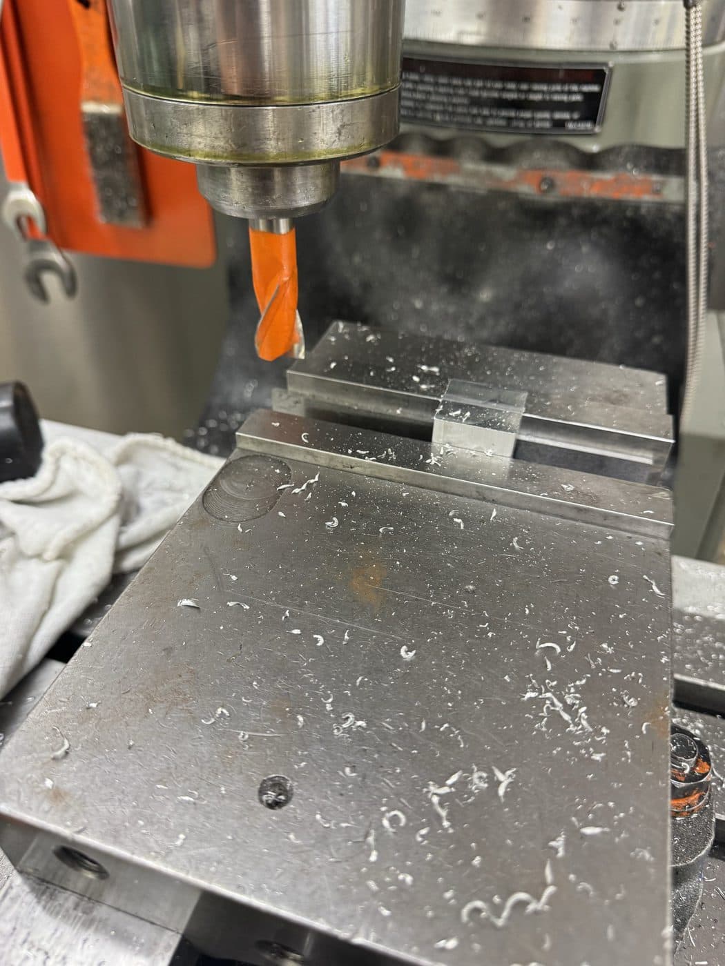 Drilling a clamped aluminium plate in the mill vise, chips clearing from the flutes.