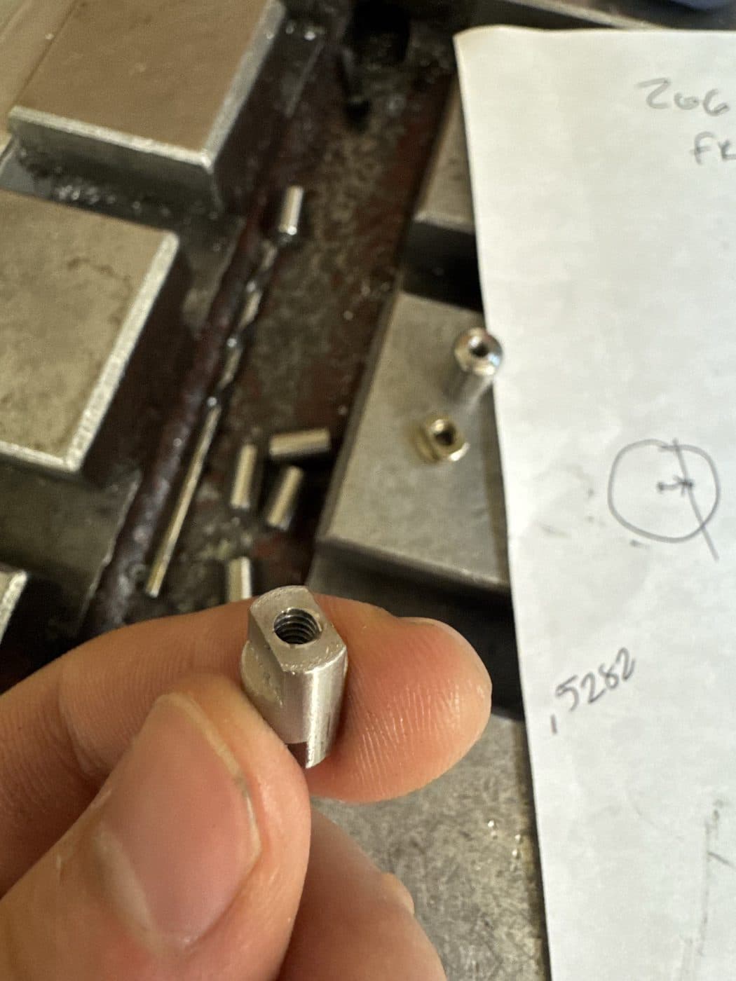 A milled and tapped part held against a hand-written dimension of 0.5282 inches.