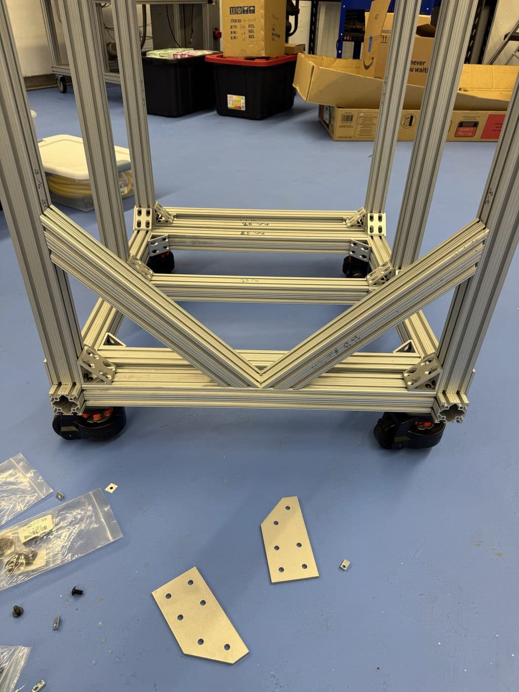 Building the 80/20 extrusion frame that carries two vacuum chambers, the V-braced lower frame going together on castors.